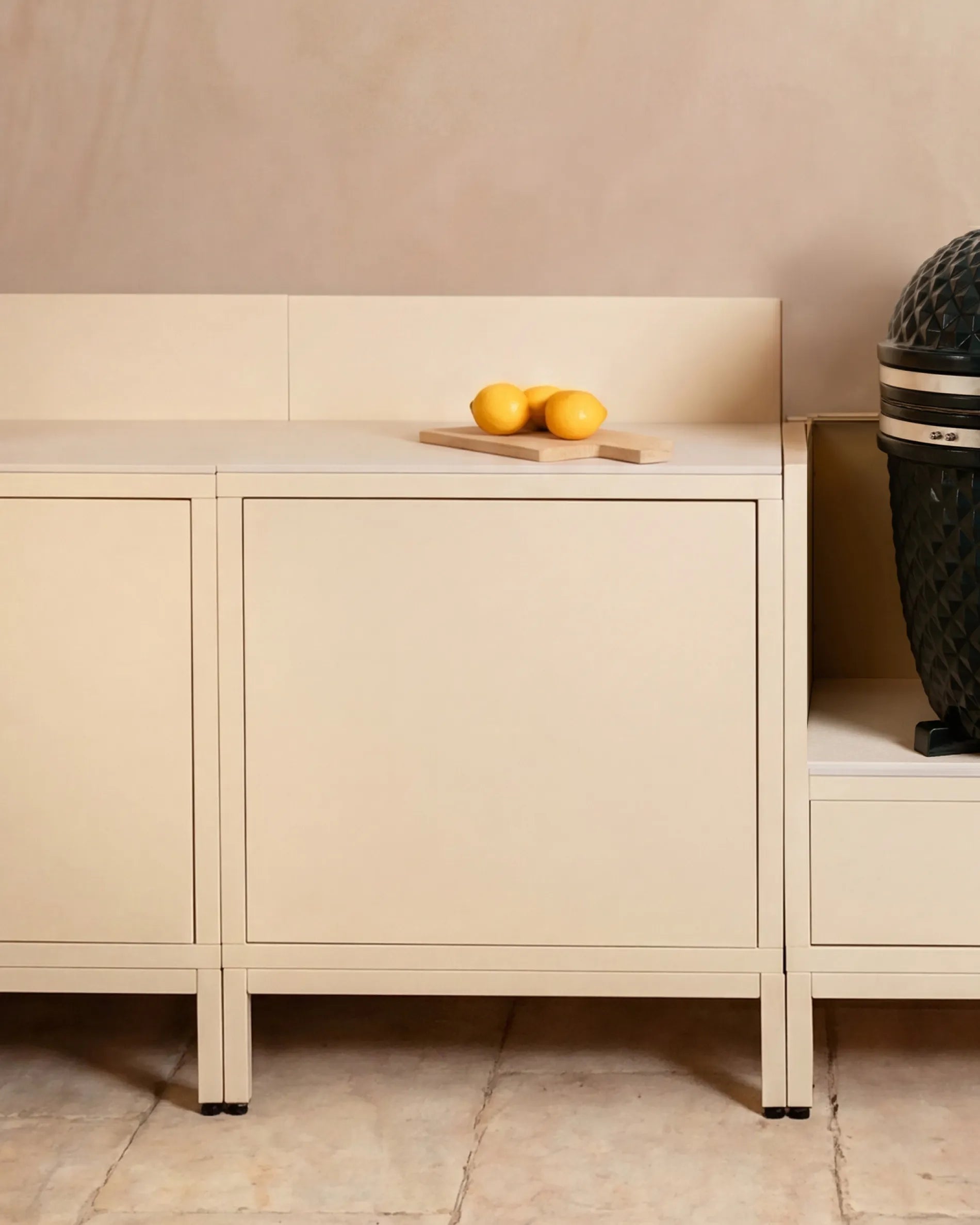 Beigefarbene Classic PILOTIS-Module für die Außenküche, mit Kamado-Grill und Zitronen auf dem Brett