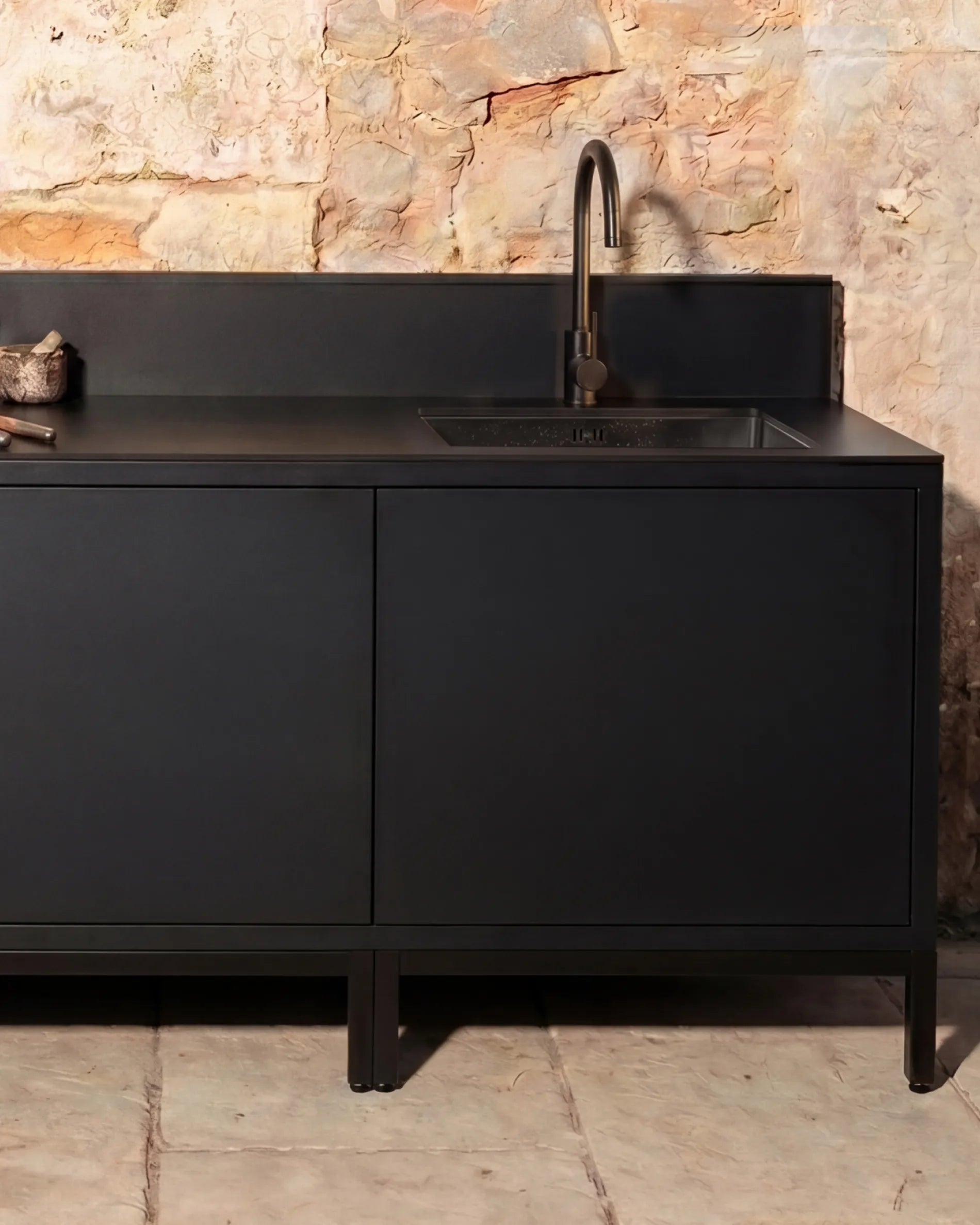 Schwarzer Eckschrank-Modul PILOTIS mit Spülbecken und Armatur, Outdoor-Küche an einer Steinmauer