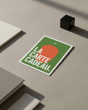 Kokko Geschenkkarte auf einer mineralischen Oberfläche, grafisches Motiv in Grün und Orange mit dem Text „die Geschenkkarte“.
