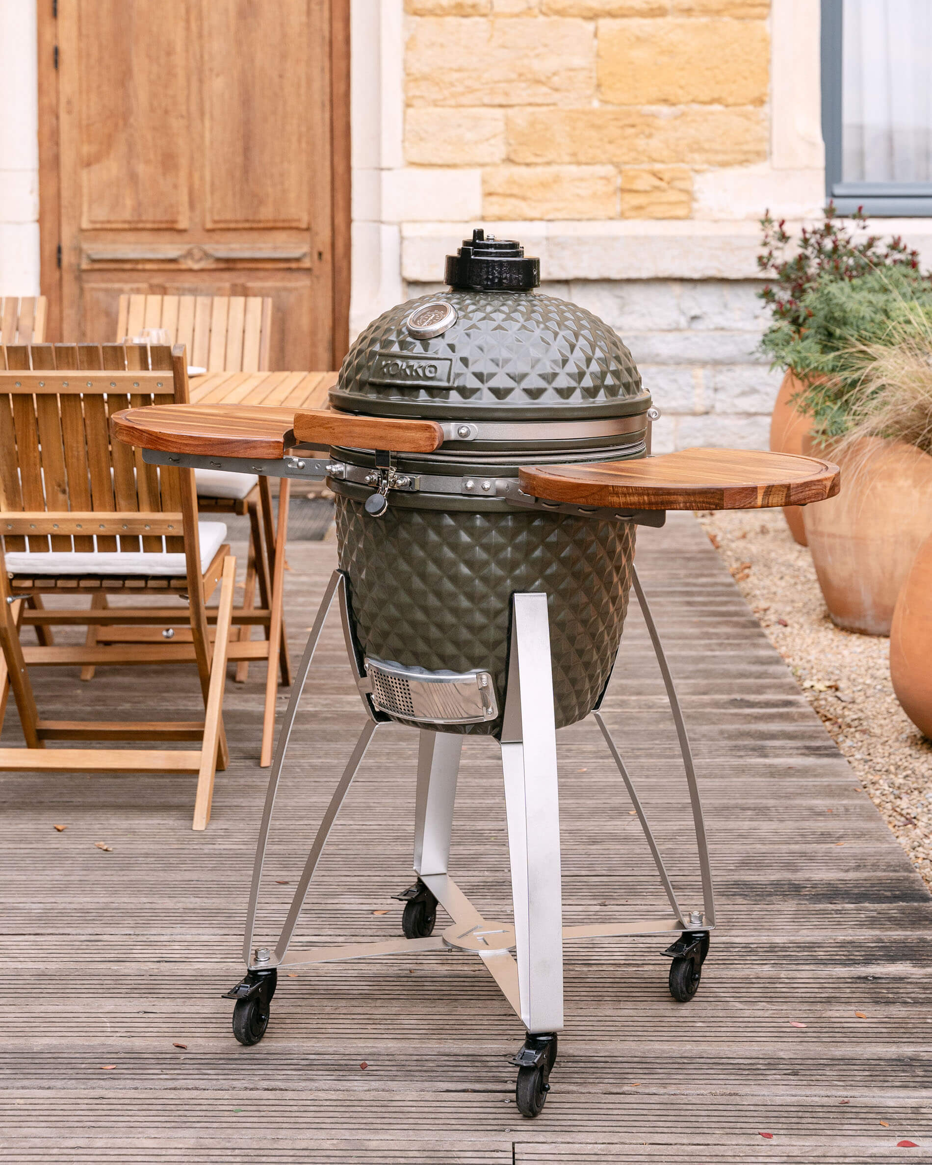 Kamado Kokko auf mobilem Wagen mit seitlichen Holzablagen, im Außenbereich auf einer Terrasse präsentiert.
