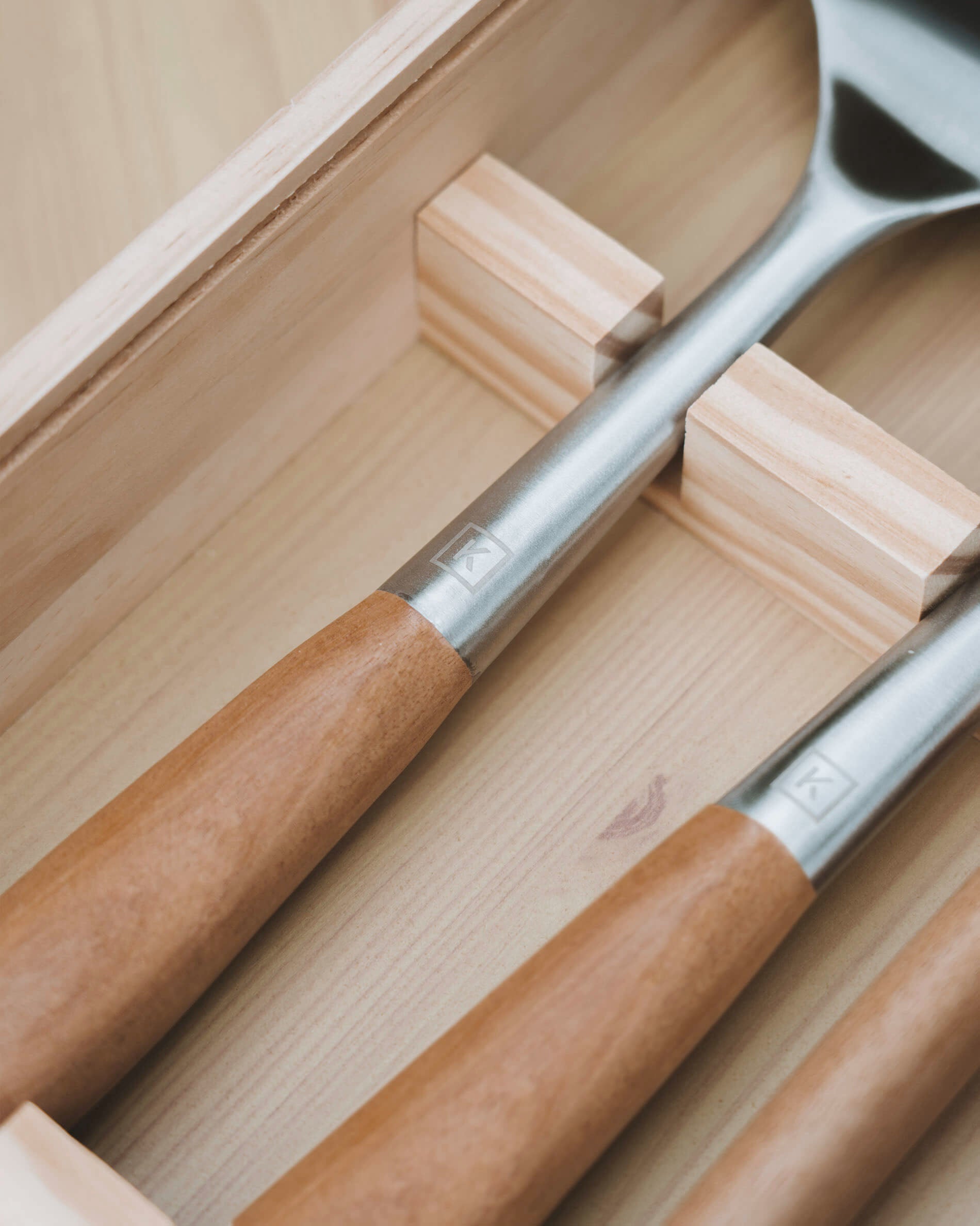 Dettaglio di utensili da cucina con manici in legno di acacia e teste in acciaio inox, riposti in una scatola di legno con scomparti