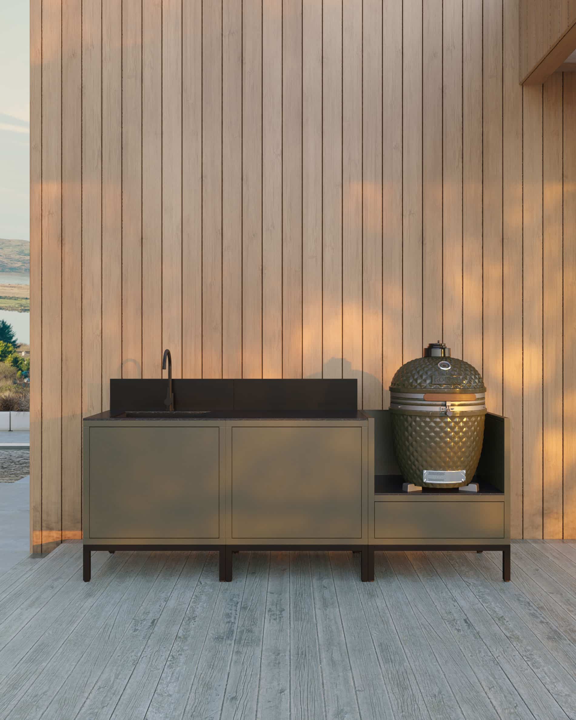 Cucina su pilotis a 3 moduli per kamado con lavello integrato, mobile color oliva con piano di lavoro e alzatina coordinati, lavello con rubinetto a sinistra, due moduli centrali chiusi per lo stoccaggio e kamado integrato nel modulo laterale destro, struttura su piedini neri, installazione all’esterno contro una parete rivestita in legno.