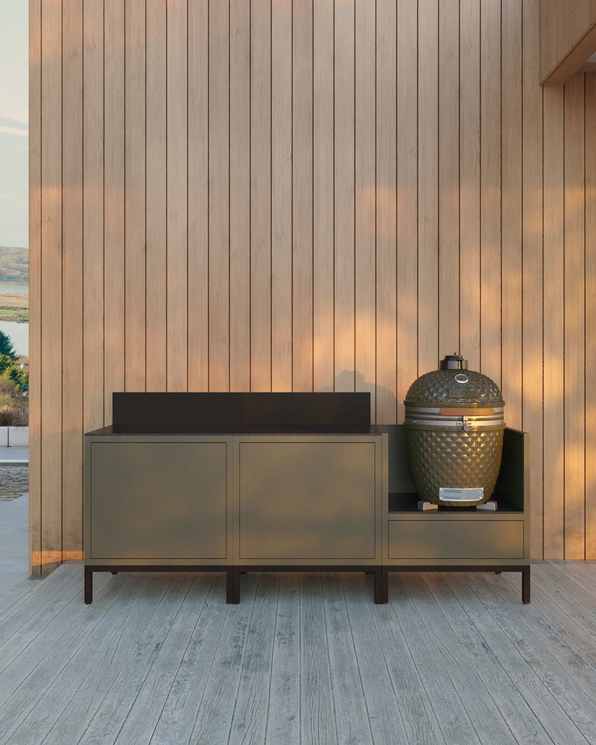Cuisine pilotis 3 modules pour kamado, meuble coloris vert olive avec plan de travail sombre et crédence assortie, deux modules de rangement fermés à gauche et kamado intégré dans le module latéral droit, structure sur pieds noirs, installation en extérieur contre un mur en bois.