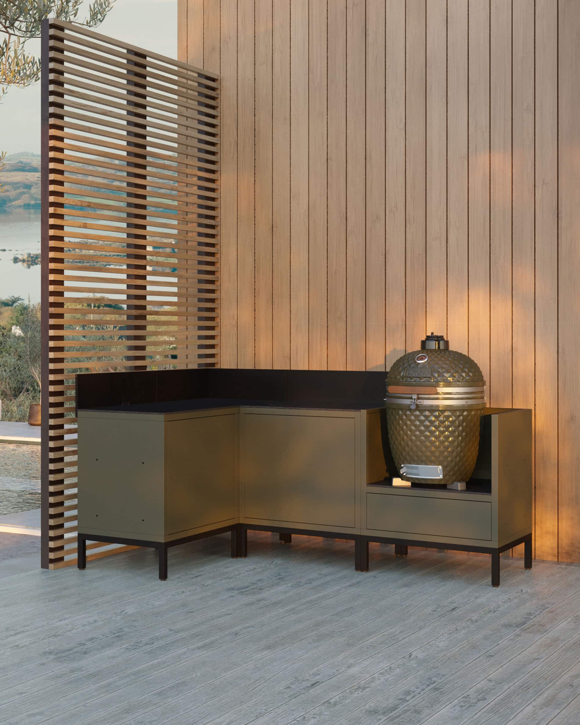Modulo cucina angolare su pilotis per kamado, composizione di mobili verde oliva con lavello integrato, piano di lavoro scuro e alzatina coordinata, kamado posizionato nel modulo laterale destro, struttura su piedini neri.