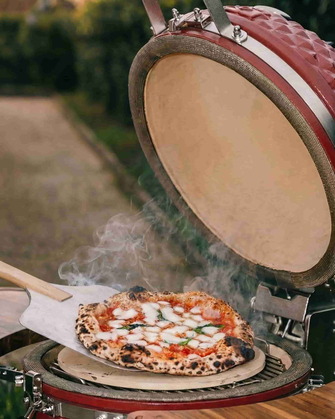 Pizza déposée sur une pierre réfractaire dans un kamado Kokko ouvert, cuisson au charbon de bois.