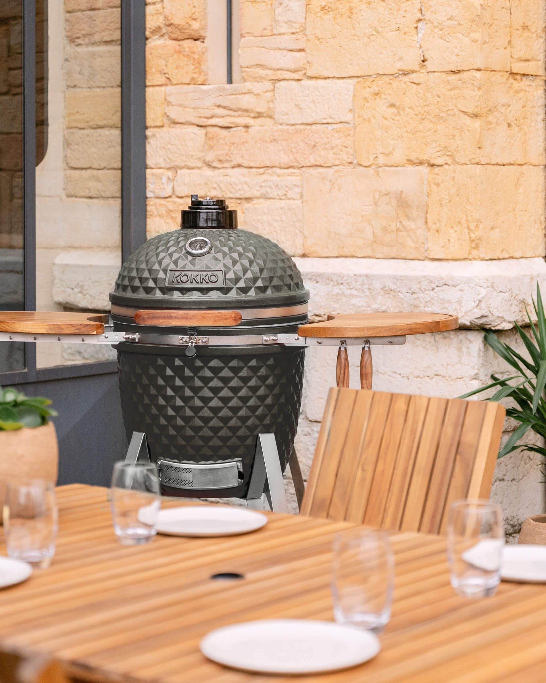 Kamado Kokko 22 pollici in ceramica verde oliva presentato su una terrazza.