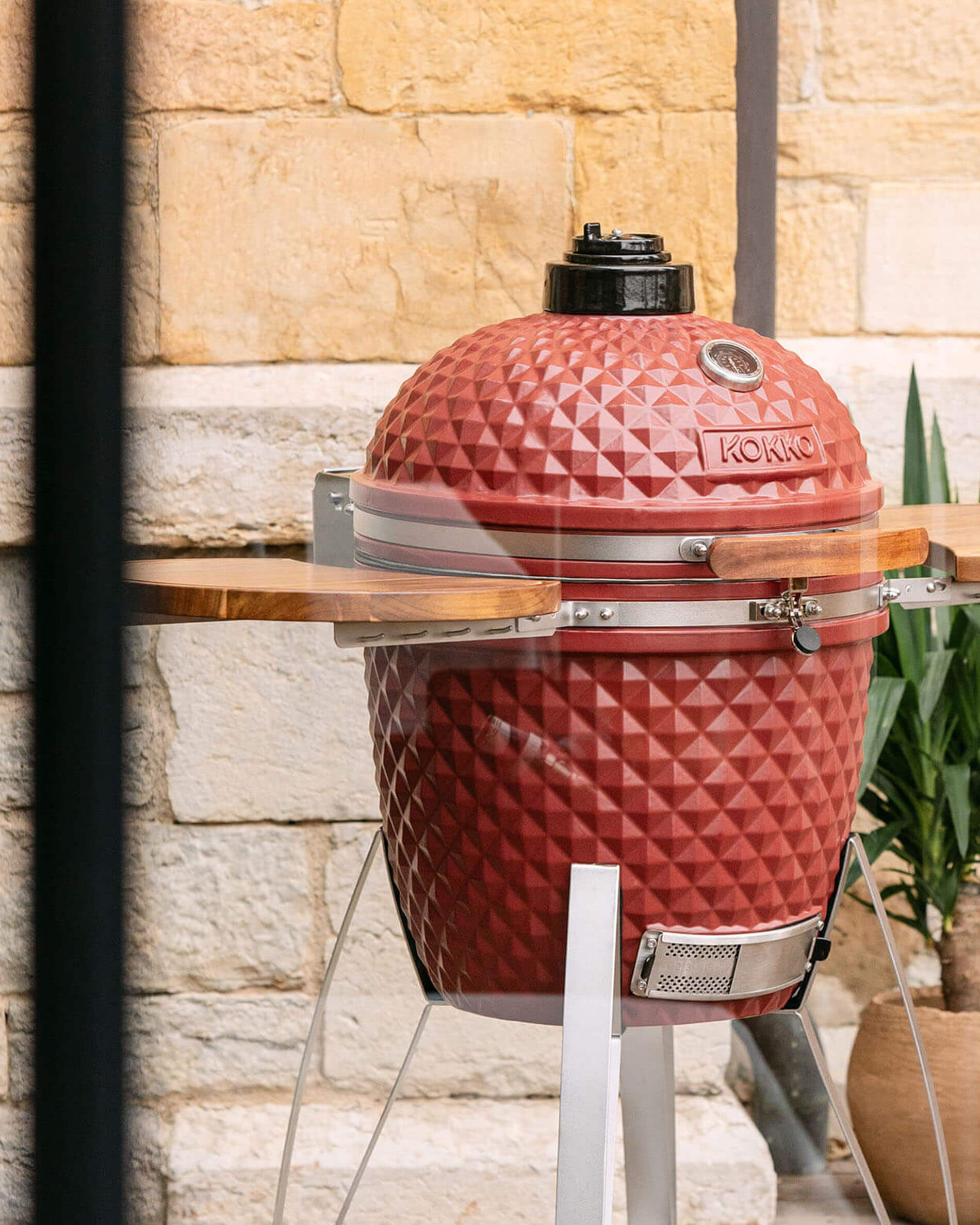 Kamado Kokko 22 pollici rosso ossido, presentato da solo all’esterno.