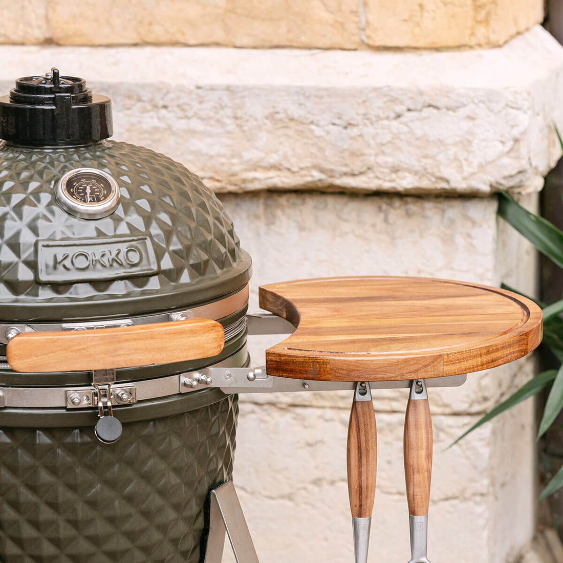 Détail du kamado Kokko équipé d’un plateau latéral en bois d’acacia et de crochets pour ustensiles.