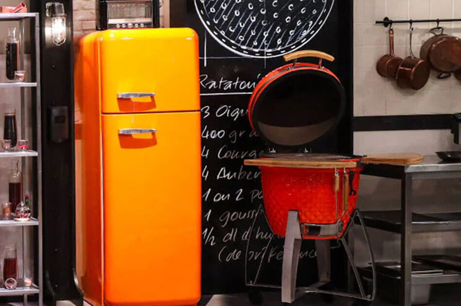 Kamado Kokko rouge en céramique installé sur le plateau de l’émission Top Chef, couvercle ouvert, avec plateaux latéraux en bois, au sein d’une cuisine professionnelle de tournage.