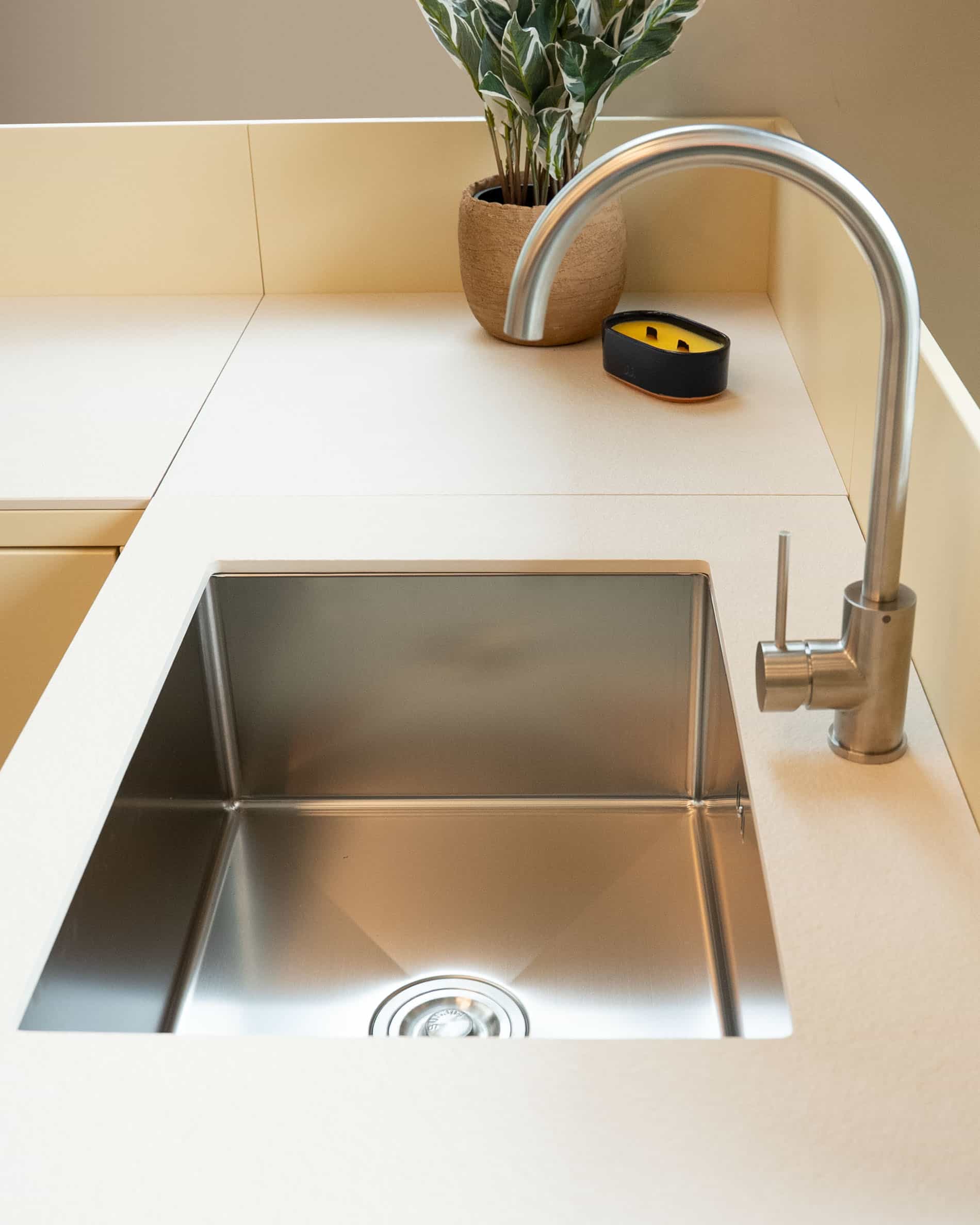 Dettaglio del lavello integrato in una cucina su palafitte, con vasca in acciaio inox, rubinetteria metallica e piano di lavoro color crema.