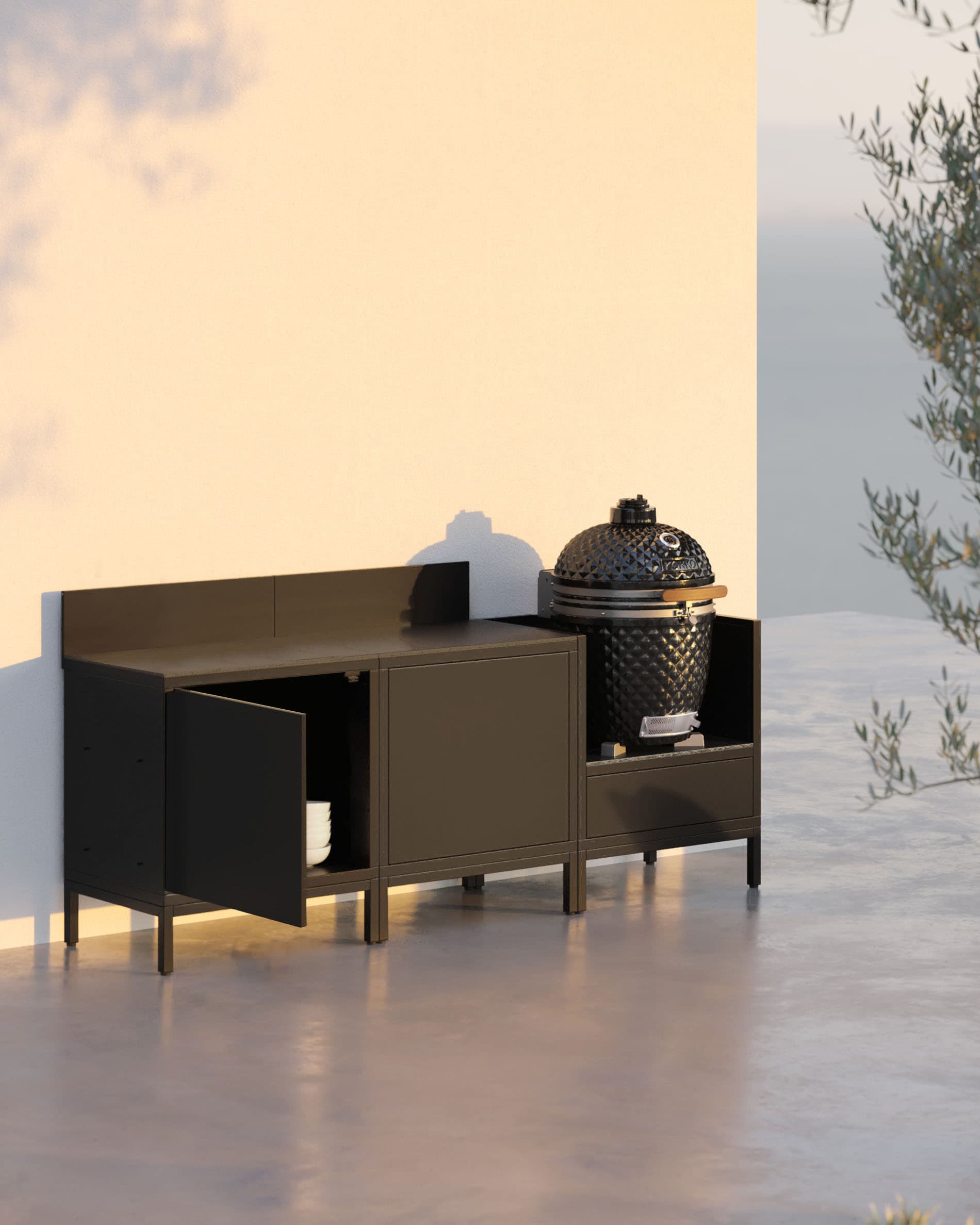 Cuisine pilotis 3 modules avec kamado, meuble noir et une porte de rangement ouverte.