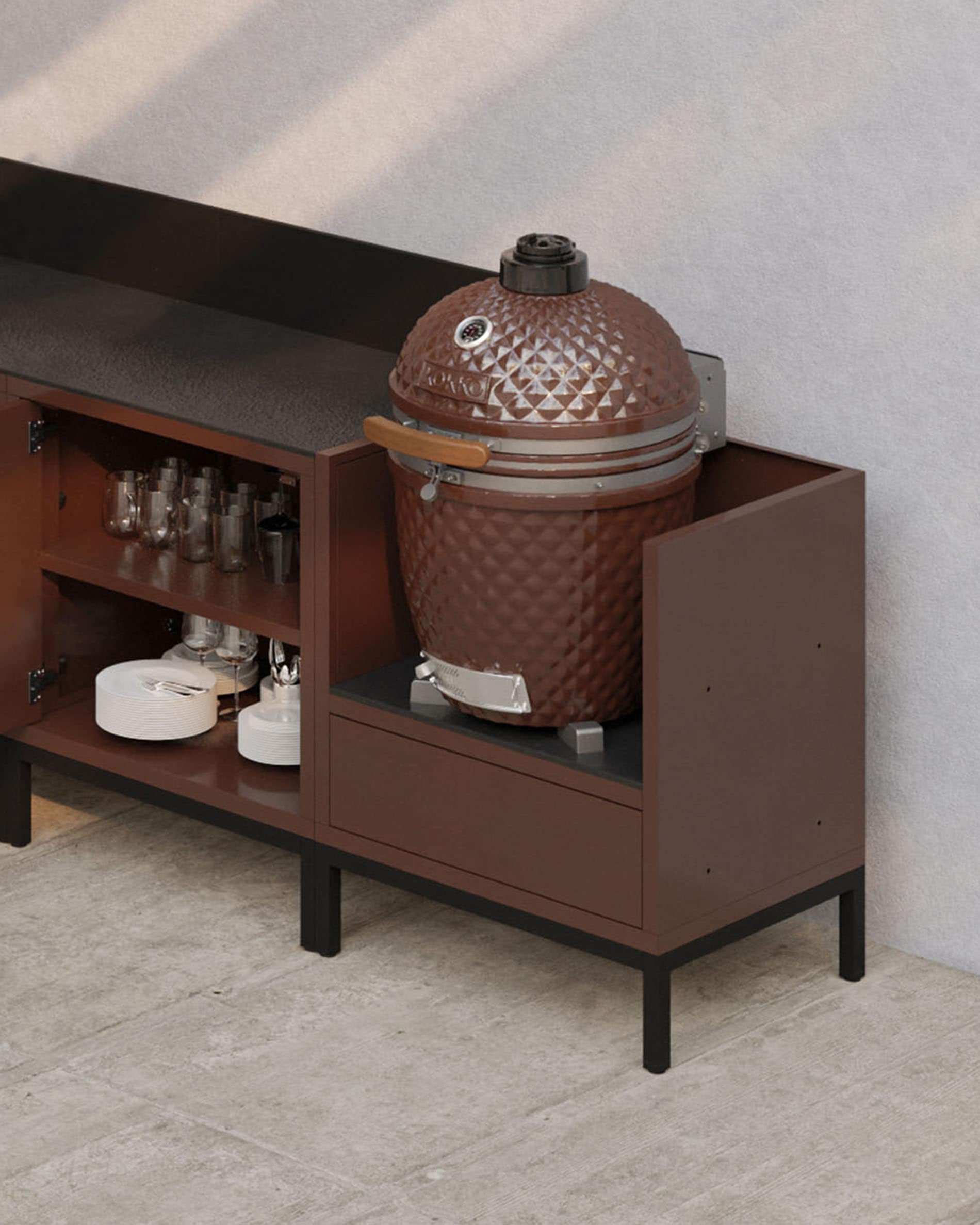 Cucina su palafitte modulare color ruggine con piano di lavoro scuro, vani a giorno e modulo progettato per ospitare un kamado.